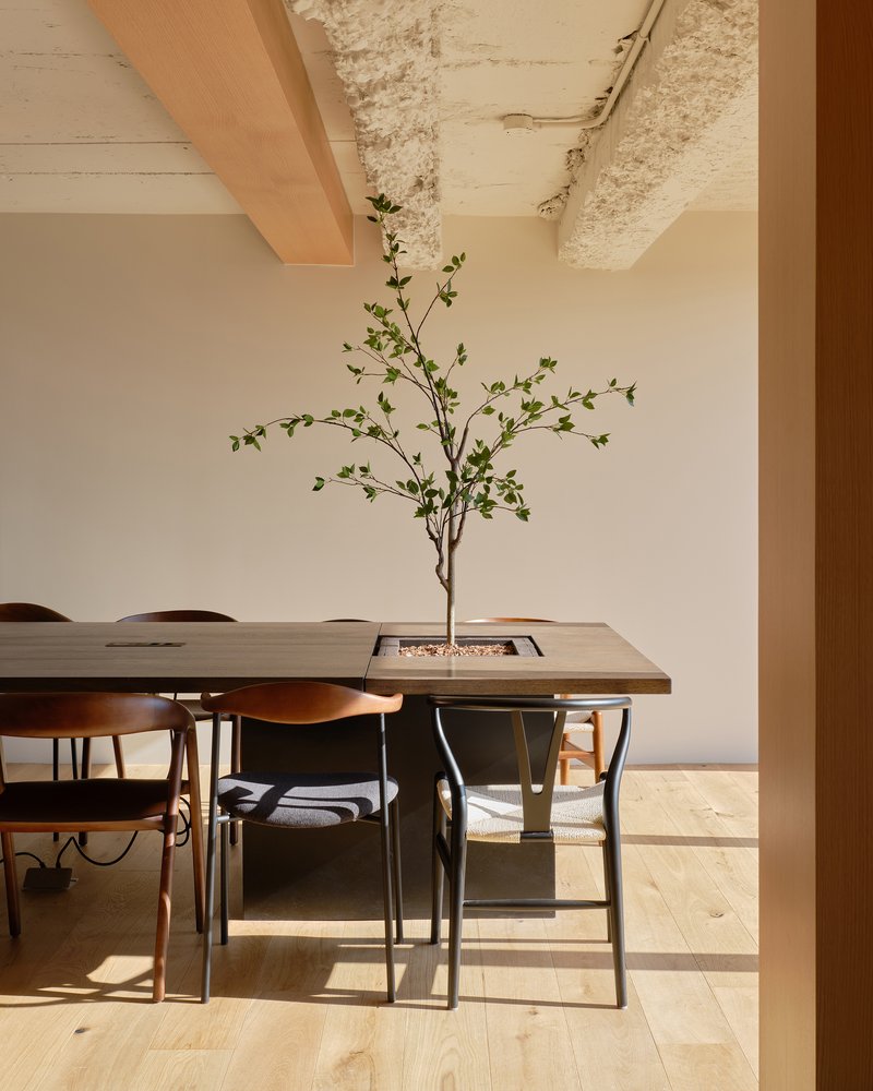 Dining table with integrated planter and branch centerpiece beneath exposed concrete ceiling