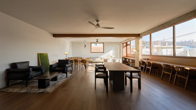 Open plan living and dining area with exposed brick wall and ribbon windows overlooking rooftops