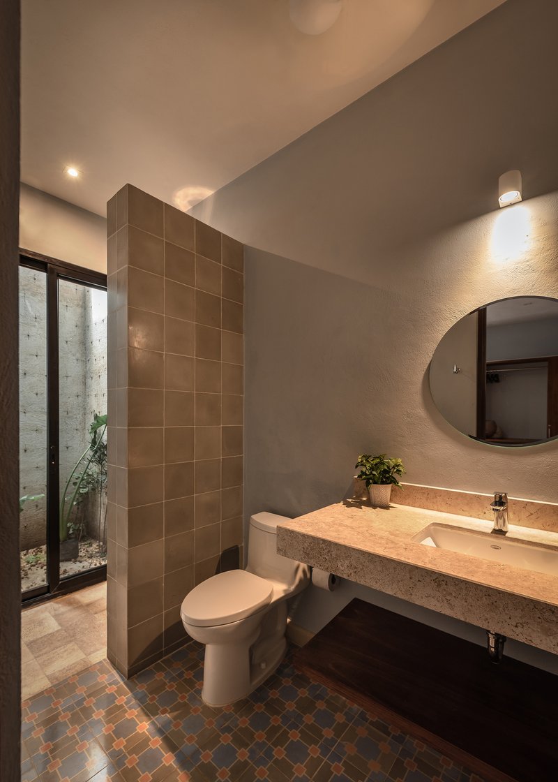 Bathroom interior with brown tile partition wall, terrazzo vanity, and view to planted courtyard through glazed door