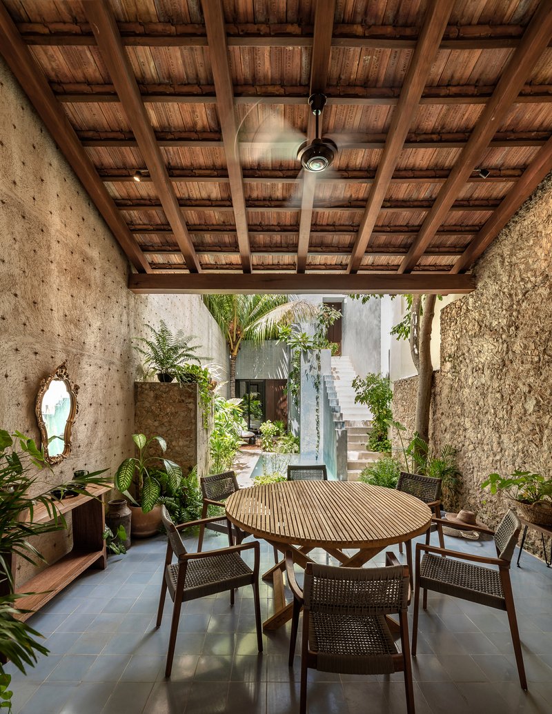Covered dining area with timber ceiling, exposed beams, ceiling fan and view to planted courtyard beyond