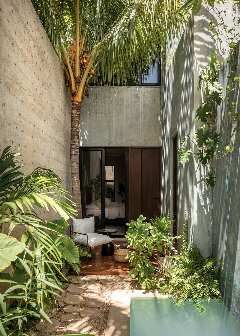 Narrow courtyard passage with stone pavers, planted beds, palm trunk and turquoise water channel