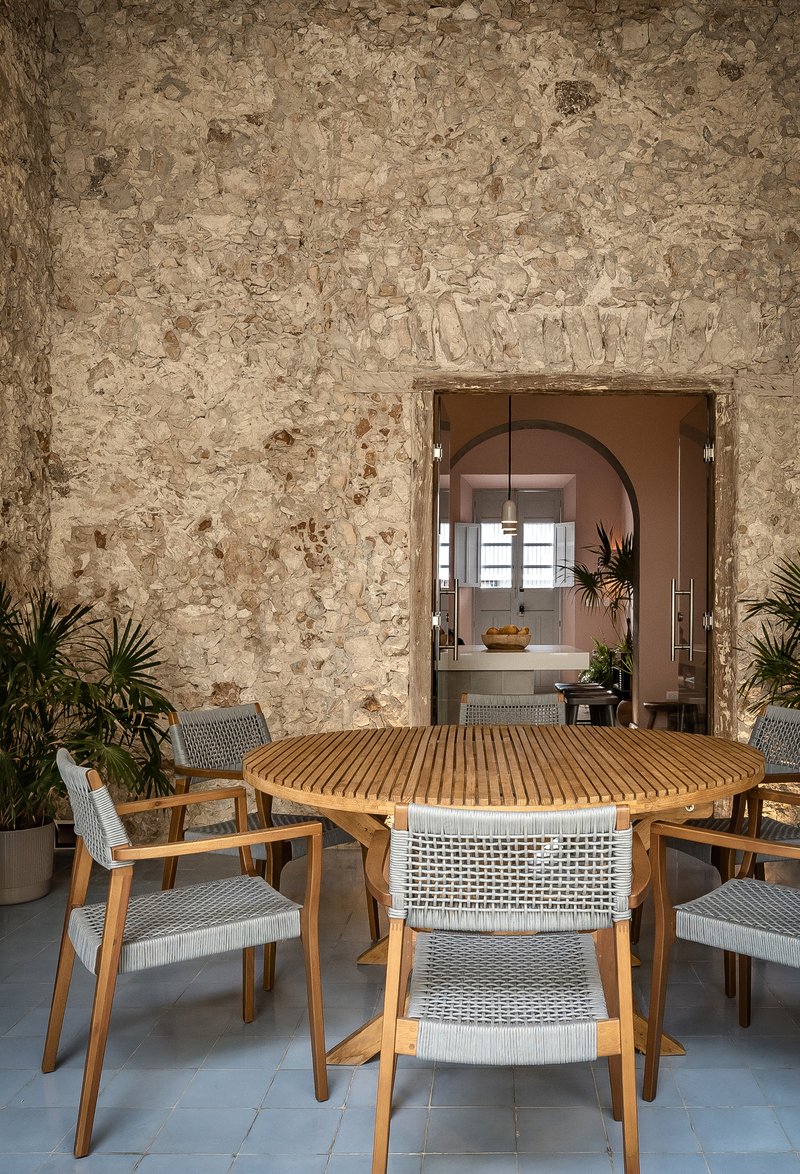 View through doorway in weathered stone wall showing dining table and arched passage beyond