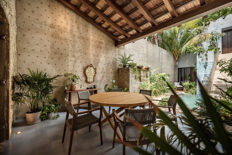 Covered outdoor dining terrace with timber beam ceiling and concrete walls opening to a planted garden