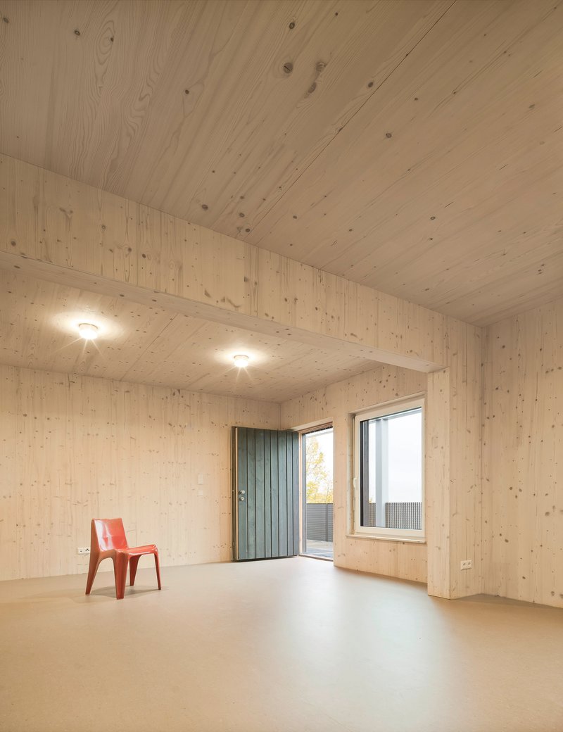 Interior room with light wood plank walls and ceiling, pale floor and a single orange chair near the window