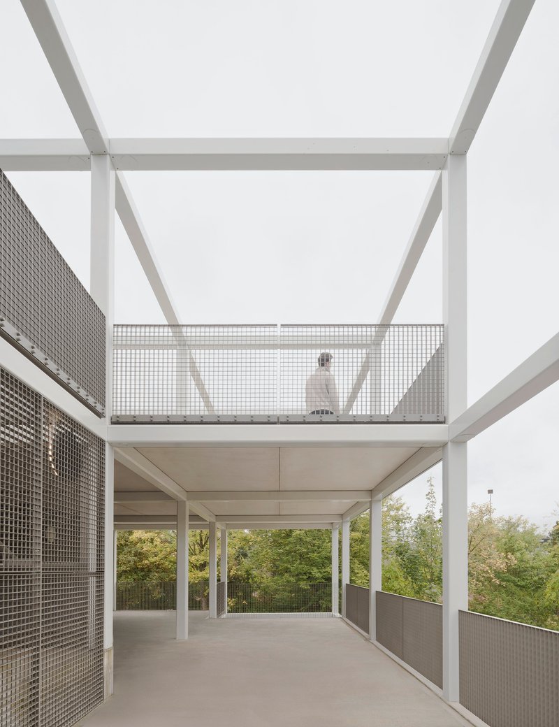 Open terrace with white steel structure and perforated metal balustrade with a figure walking on the upper level