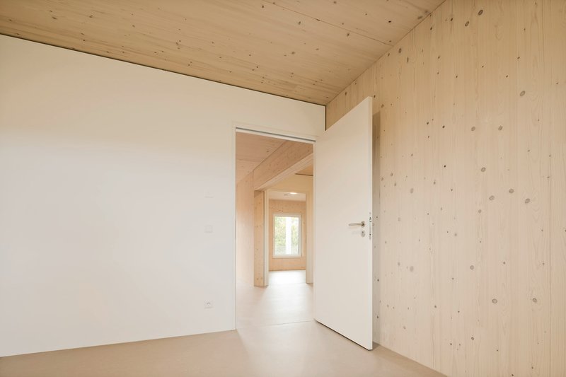 Doorway view through aligned rooms with exposed timber plank walls and white painted partitions under natural light