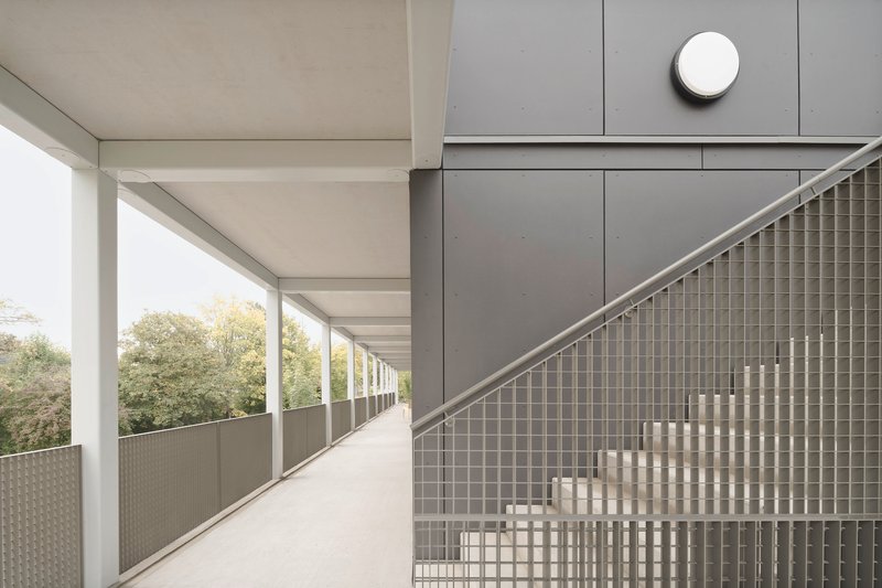 Exterior corridor with steel balustrade of woven metal mesh and gray panel cladding under overcast sky