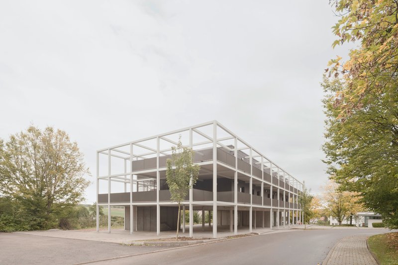 Corner view of the white steel frame structure with infill panels among deciduous trees