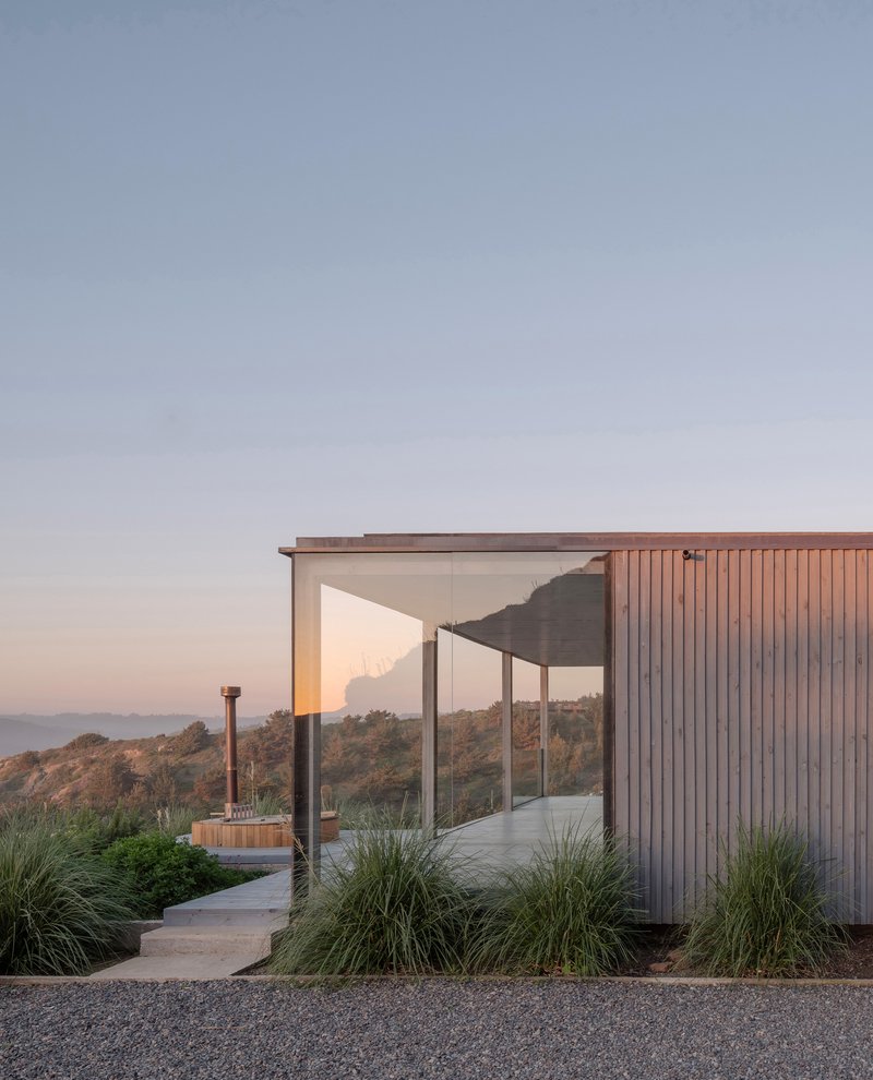 Curved concrete pathway leading to covered terrace with vertical timber cladding and ornamental grasses at sunset