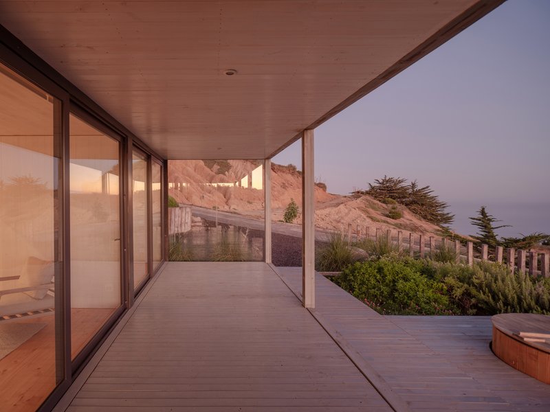 Covered timber deck with sliding glass walls overlooking terraced hillside and planted beds at dusk