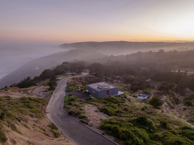 Drone view of the dwelling perched on the hillside with winding road and coastal fog at sunrise