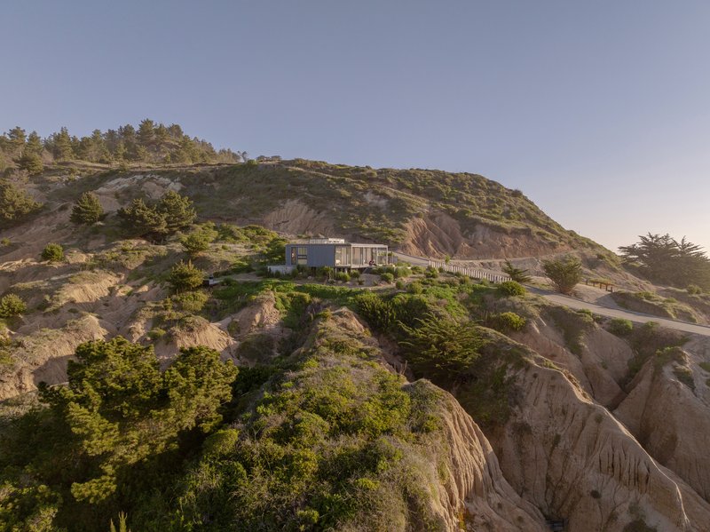 Long view of the house positioned on the eroded hillside ridge among scrub vegetation and exposed rock