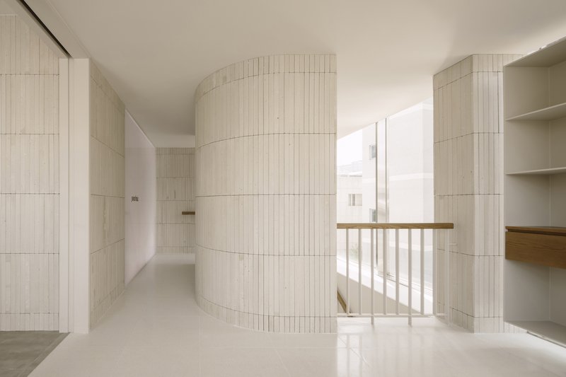 Curved ribbed tile volume around window opening with timber railing and daylight streaming in