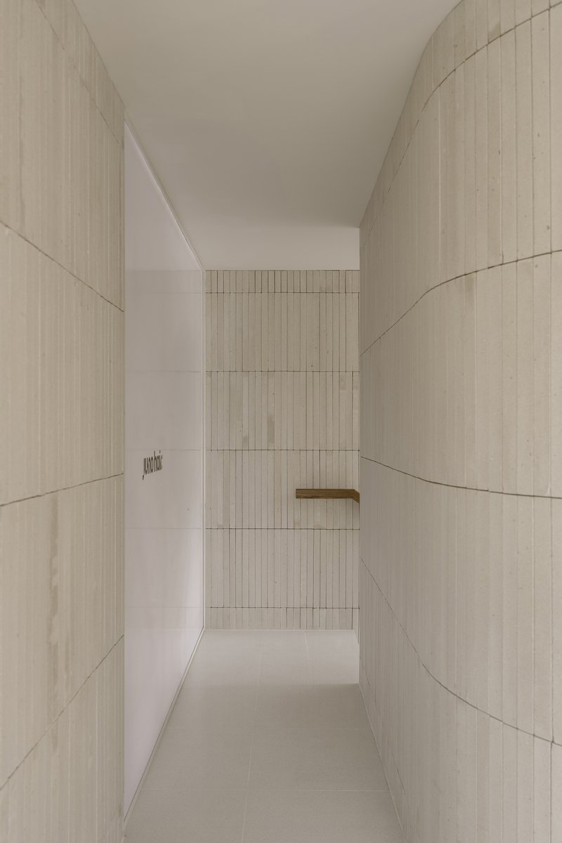 Narrow corridor flanked by curved ribbed tile walls leading to distant timber handrail