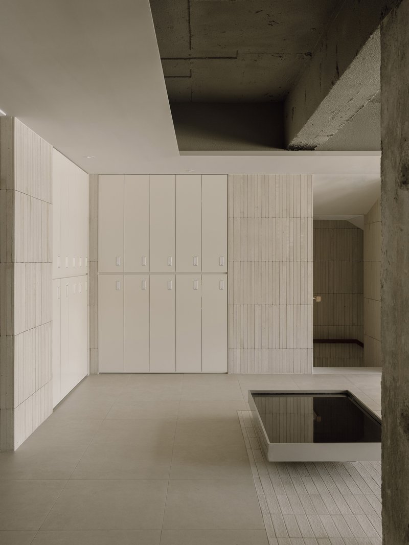Interior view of pale tiled walls and exposed concrete ceiling framing a double-height salon space