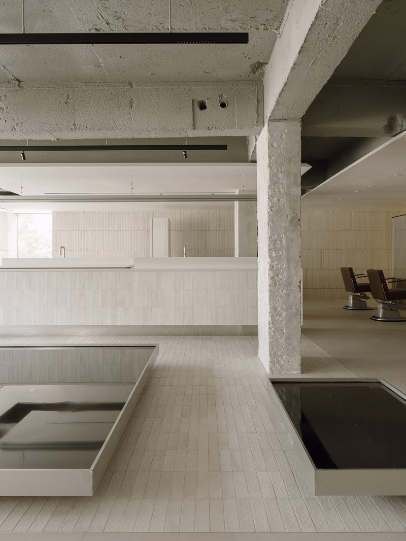 Concrete columns and exposed ceiling beams above linear salon counters clad in cream tile