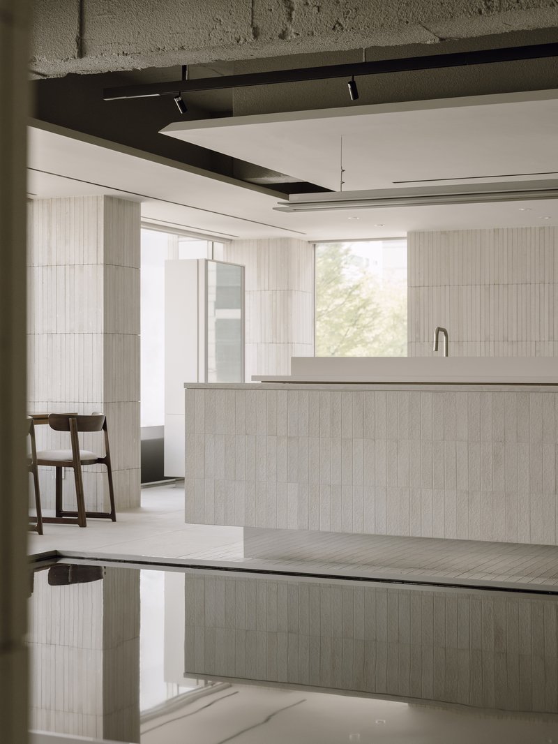 Salon workspace with light wood island and reflective dark water feature below exposed concrete beams