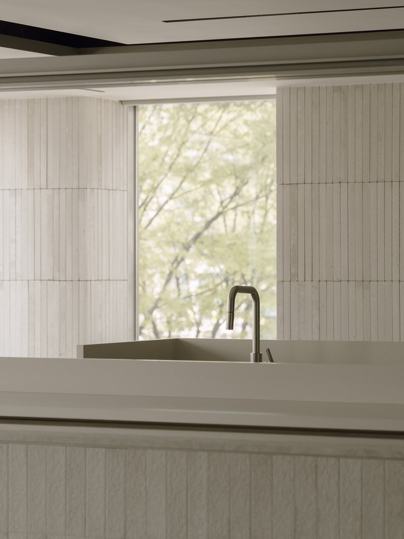 Kitchen island with integrated sink and tall faucet framed by vertical timber paneling and soft daylight