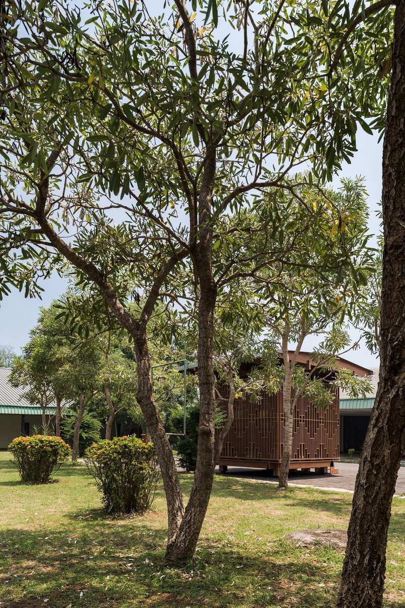 Distant view of the timber pavilion through a grove of trees on a lawn