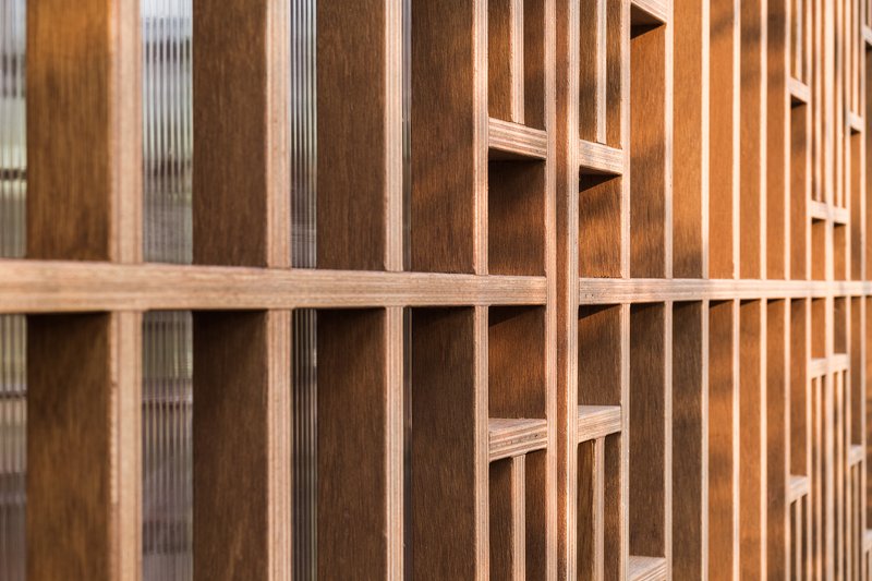 Close view of layered timber lattice screen showing alternating wood tones and translucent inserts
