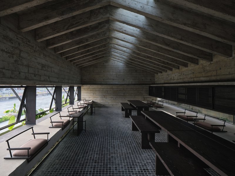 Interior hall with exposed timber ceiling beams, board-formed concrete walls and rows of benches