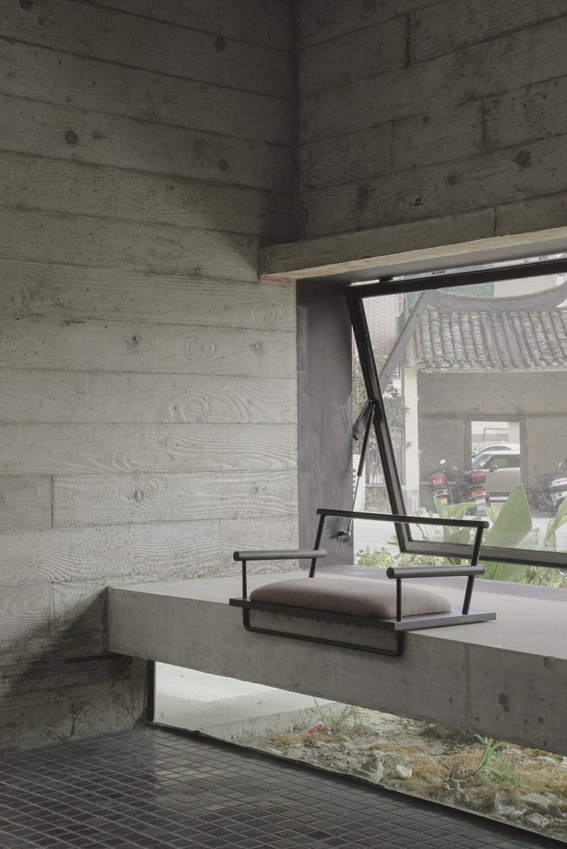 Concrete bench seat beneath board-formed walls and angled window framing planted courtyard beyond