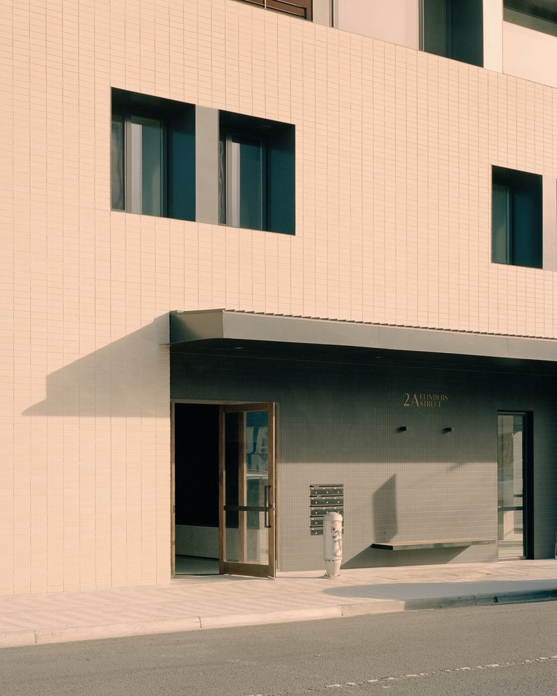 Ground-level entrance with recessed glazing and a canopy cutting into the tiled facade in afternoon sun