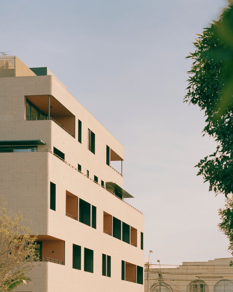 Upper floors of the cream tile facade with staggered terraces framed by foliage