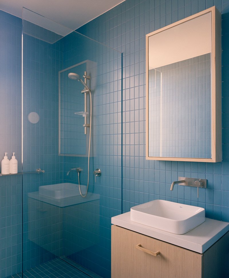 Bathroom with pale blue rectangular tile walls, glass shower enclosure and wall-mounted mirror cabinet