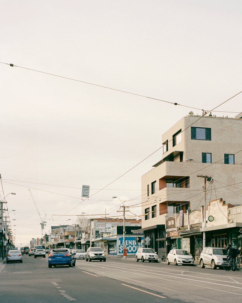 Stepped concrete facade on a corner site amid overhead tram wires and street traffic
