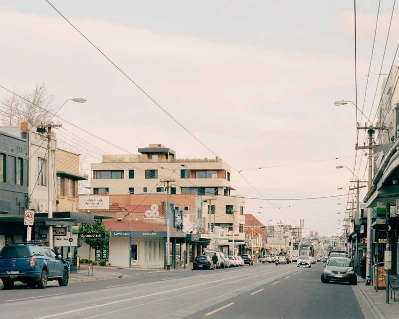 Street view of the multi-storey building rising above low-rise shopfronts beneath a network of tram cables
