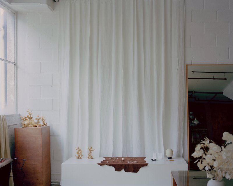 White-painted exhibition room with floor-to-ceiling curtain divider and copper planter beside the window