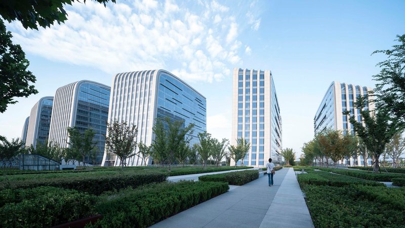 Pedestrian pathway through manicured hedges leading toward the towers under a blue sky with clouds