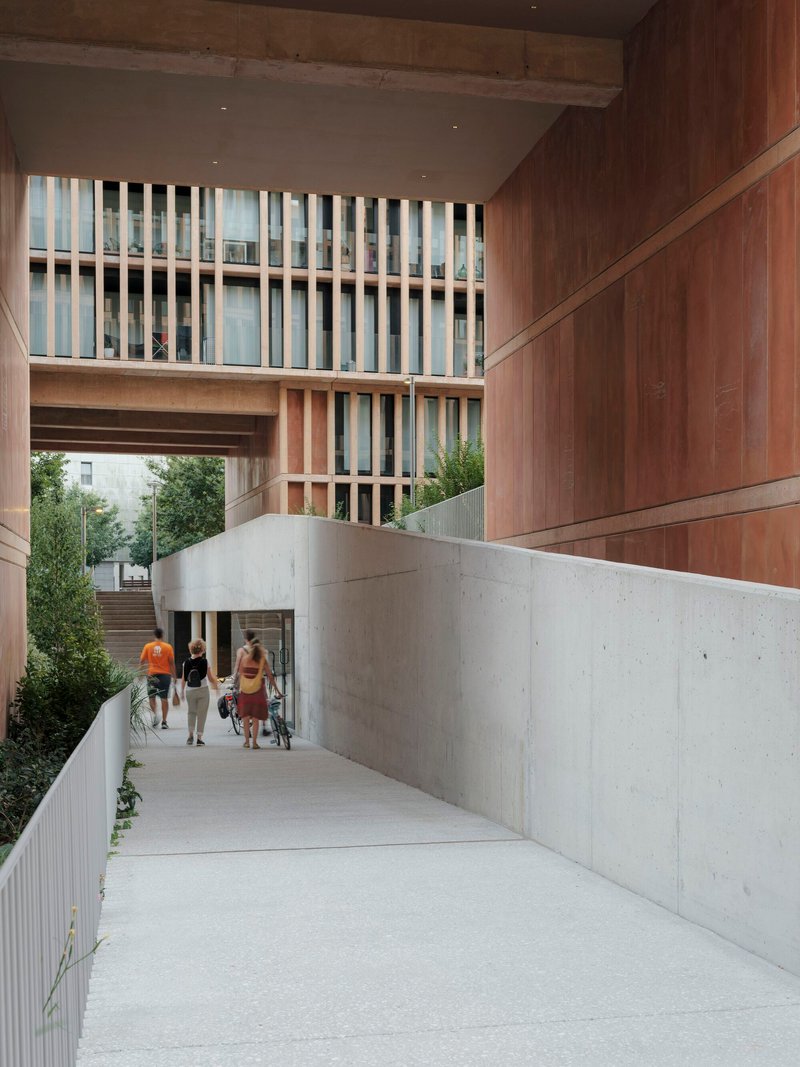 Sloped concrete passage with timber-clad soffit overhead and pedestrians approaching the walkway