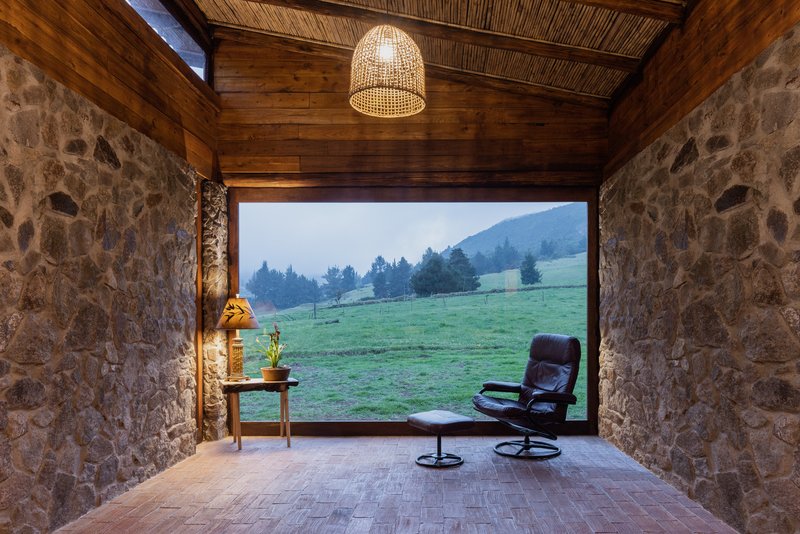 Interior room with fieldstone walls and woven ceiling framing a large opening to misty green pasture at dusk