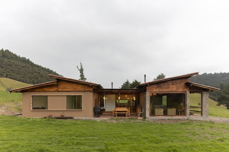 Rear elevation showing interconnected timber roof volumes over stucco and glass walls facing rolling meadows and forest