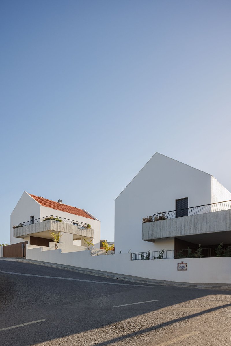 Corner view showing two white gabled volumes with concrete balconies and orange clay tile roofs from the street
