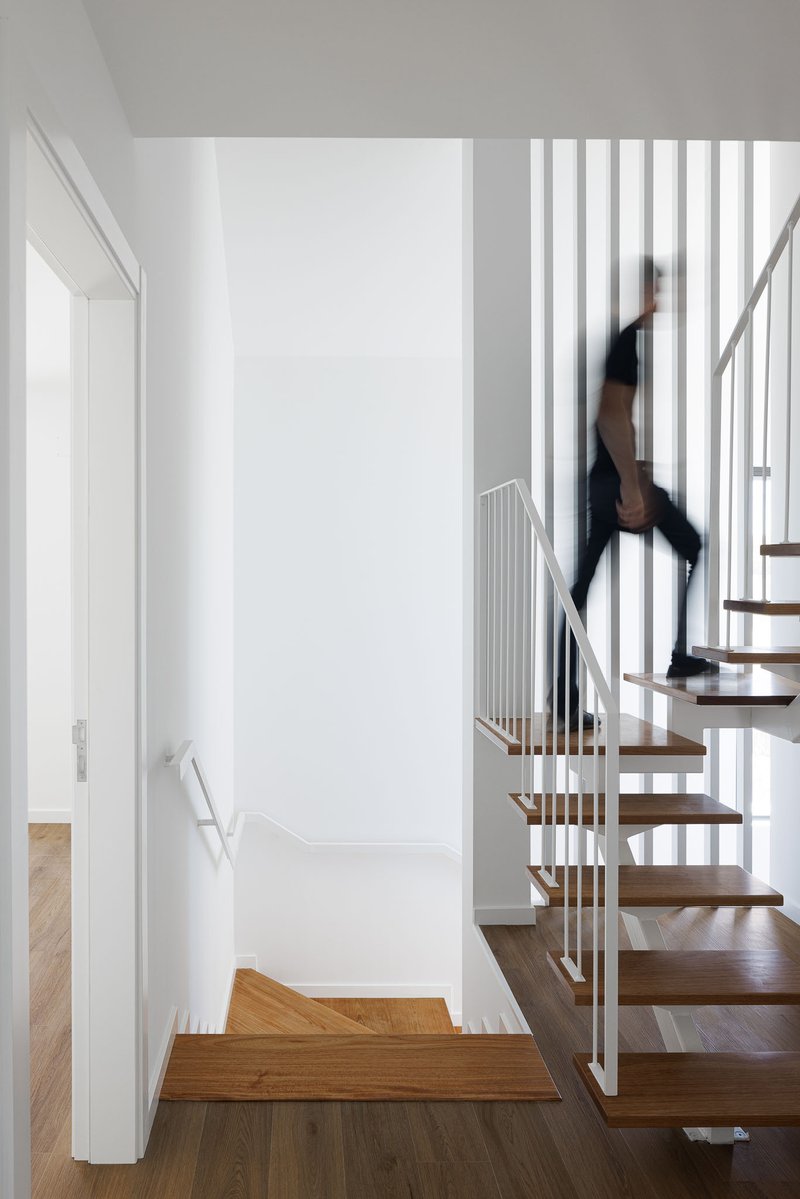 Open timber staircase with vertical white metal balusters and figure in motion ascending the treads