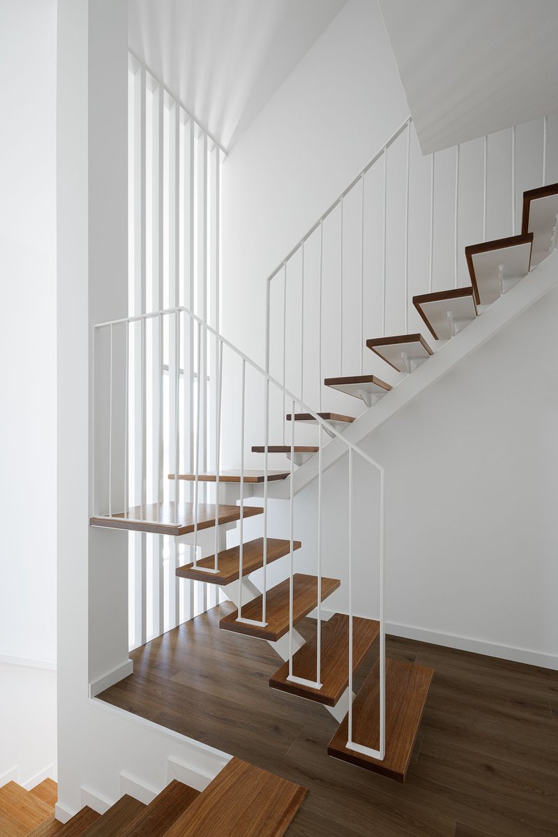 Open-tread staircase with timber treads and white steel frame between vertical balustrade panels