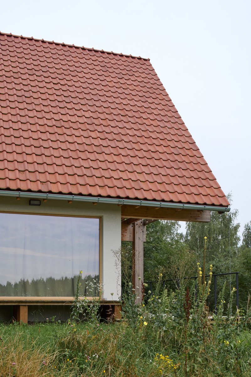 Steep terracotta tile roof above a glazed corner with tall grasses and wildflowers in the foreground