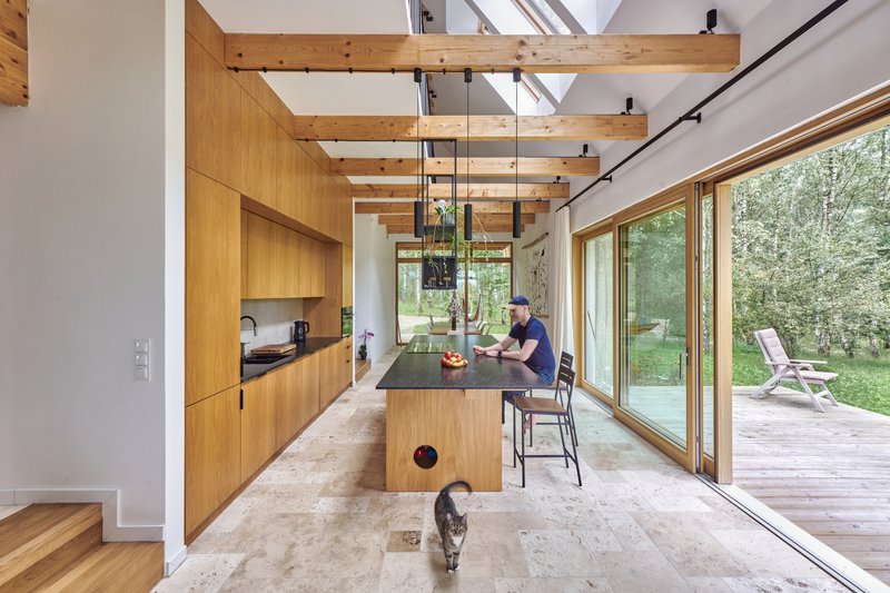 Open kitchen with wood cabinetry and exposed timber beams leading to sliding glass doors and terrace beyond