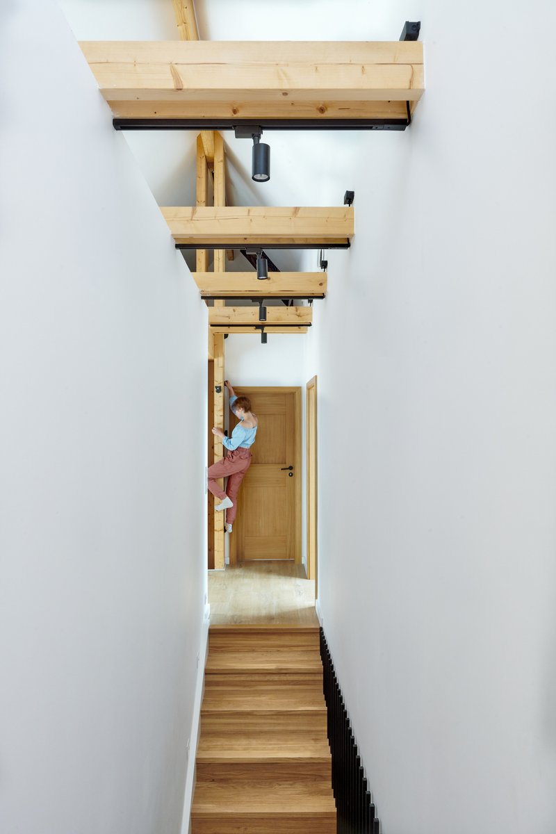 Vertical view up the timber stairwell with exposed beams and a figure pausing at the landing