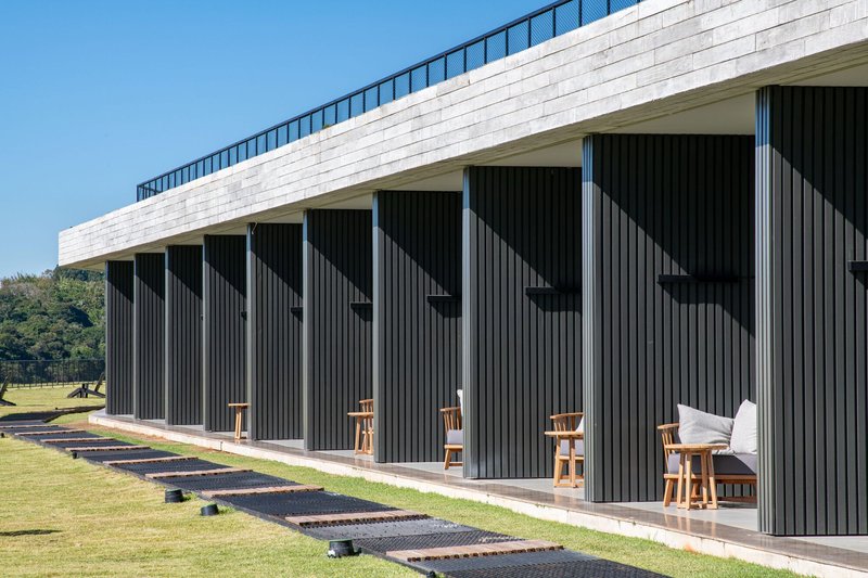 Repeating terrace openings framed by vertical dark cladding beneath a white horizontal roof parapet under clear sky