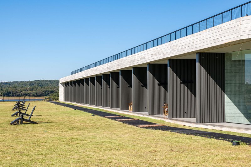 Facade with vertical timber battens below a white brick parapet and sloped green roof under clear sky