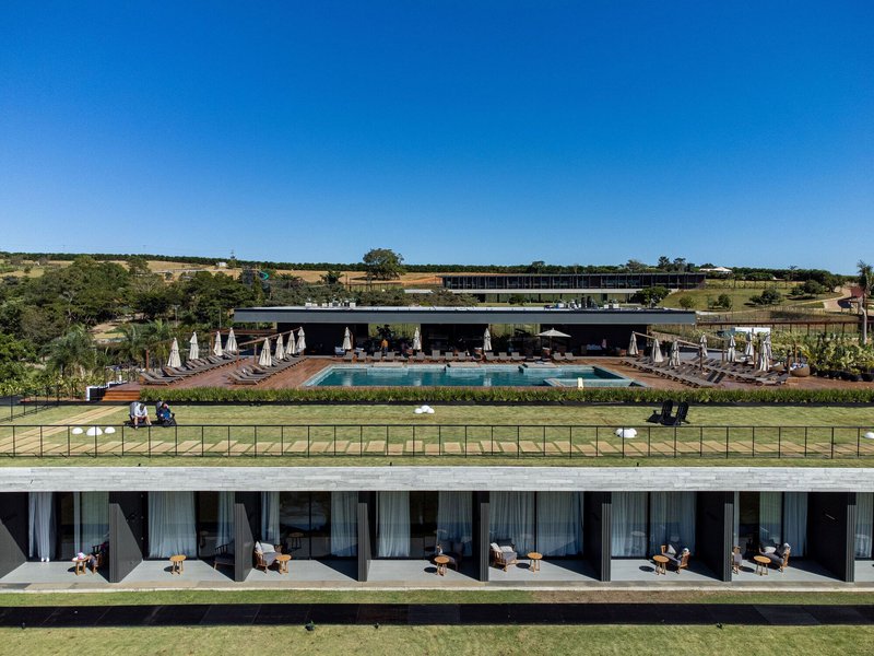Terraced deck with pool loungers and planted hedges descending toward guest room balconies below green lawn