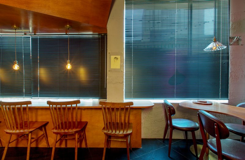 Seating alcove with horizontal blinds and wooden chairs arranged along a curved bar counter
