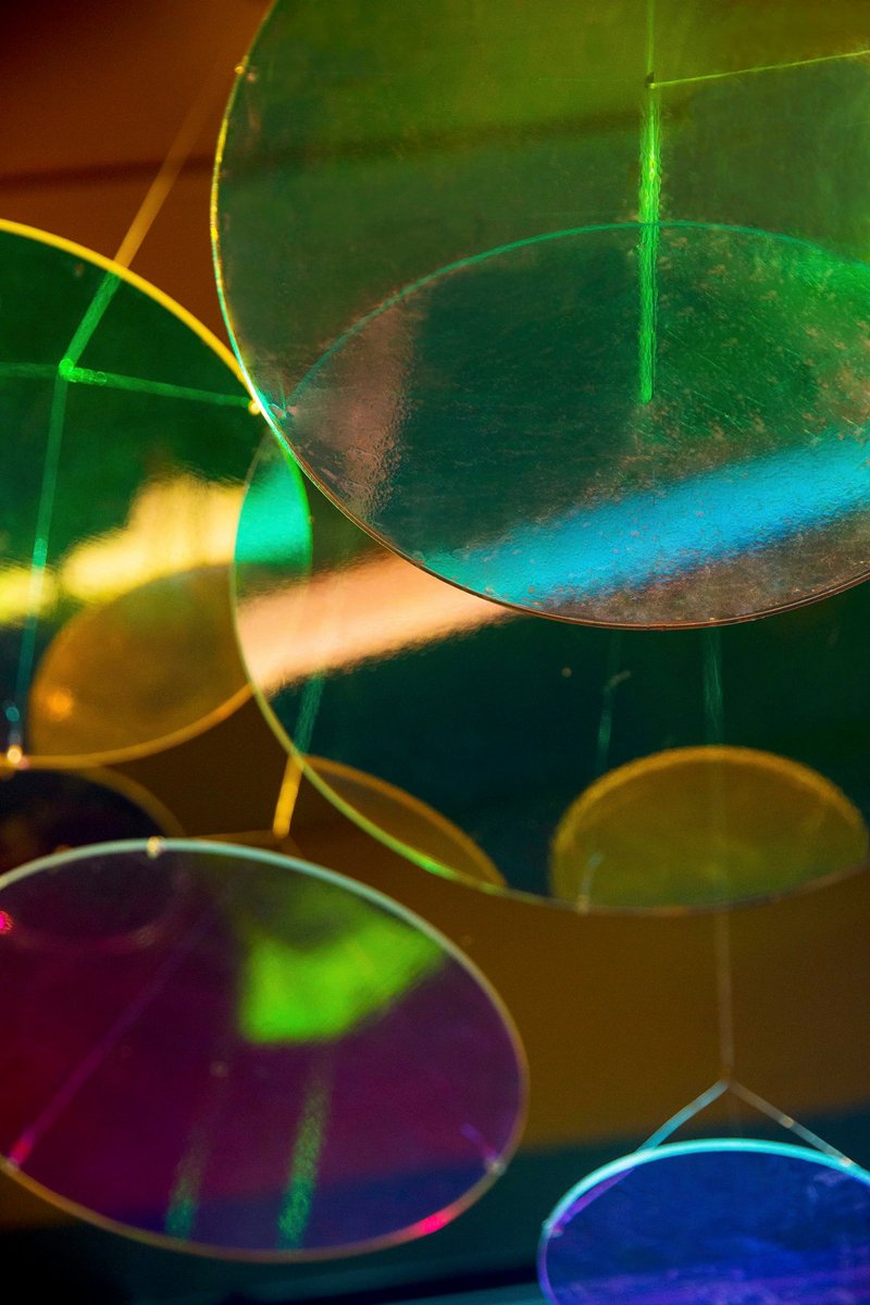 Close-up of overlapping translucent colored glass discs casting layered green, purple, and amber light reflections