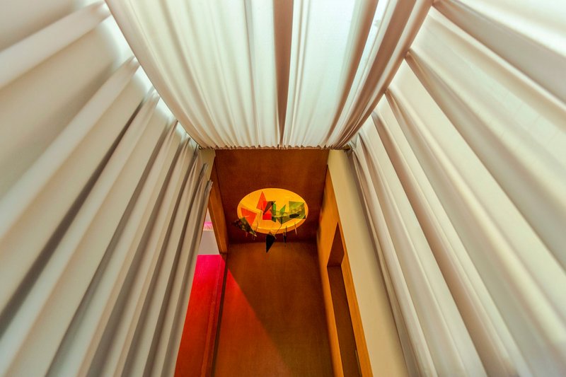 Overhead view down a narrow stairwell with white pleated fabric walls and colored glass disc installation below