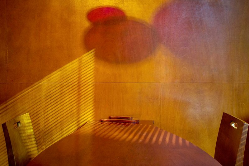 Corner alcove with timber paneling showing striped afternoon sunlight patterns through horizontal blinds and colored light shadow above