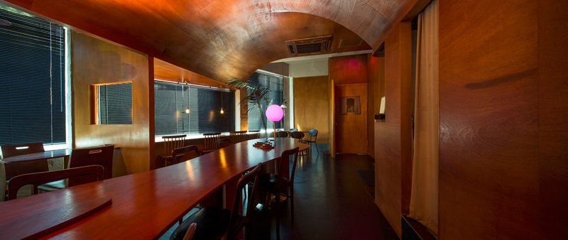 Panoramic dining hall with barrel-vaulted timber ceiling, horizontal blinds, and long wooden tables lit by pink globe lamp